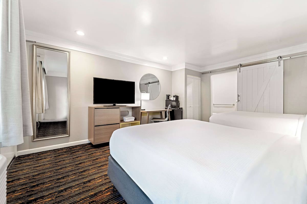 Ein Hotelzimmer mit einem großen Bett, einem Flachbildfernseher, einem Schreibtisch mit Stuhl, einem Spiegel und einem Kleiderschrank.
