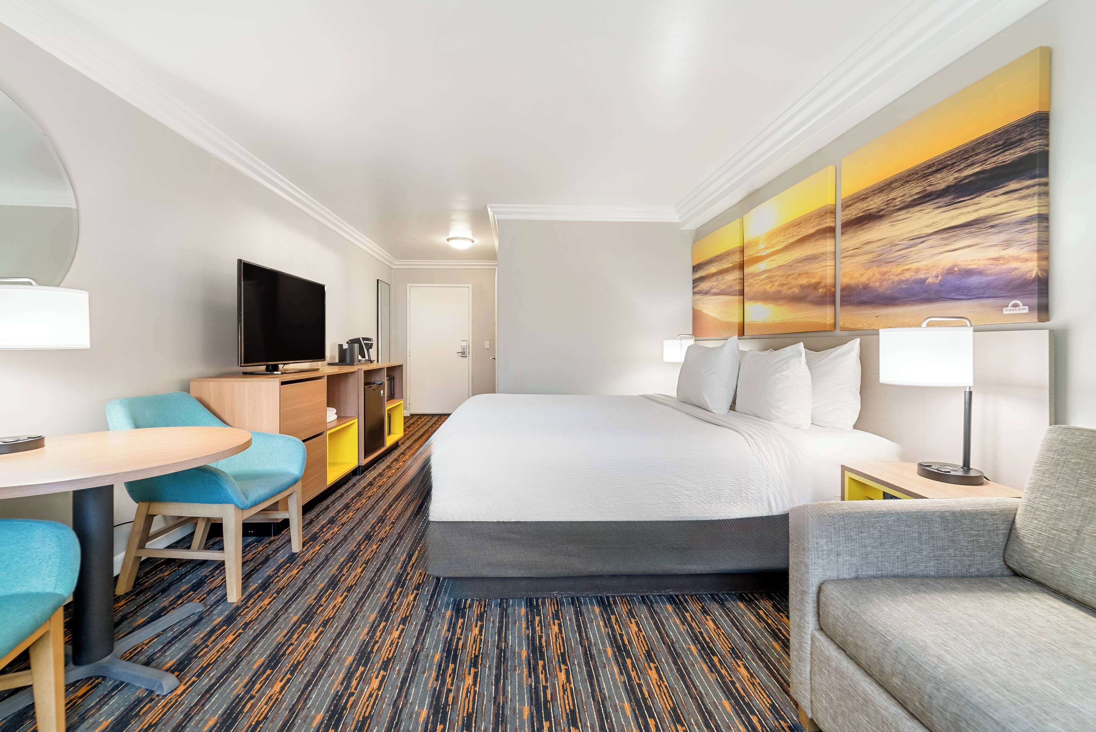 Une chambre d’hôtel avec un grand lit, une télévision, un bureau avec une chaise et un tableau au mur.