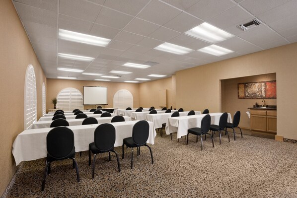 Une salle de conférence équipée de plusieurs tables et chaises, d’un écran de projection et d’un coin cuisine.