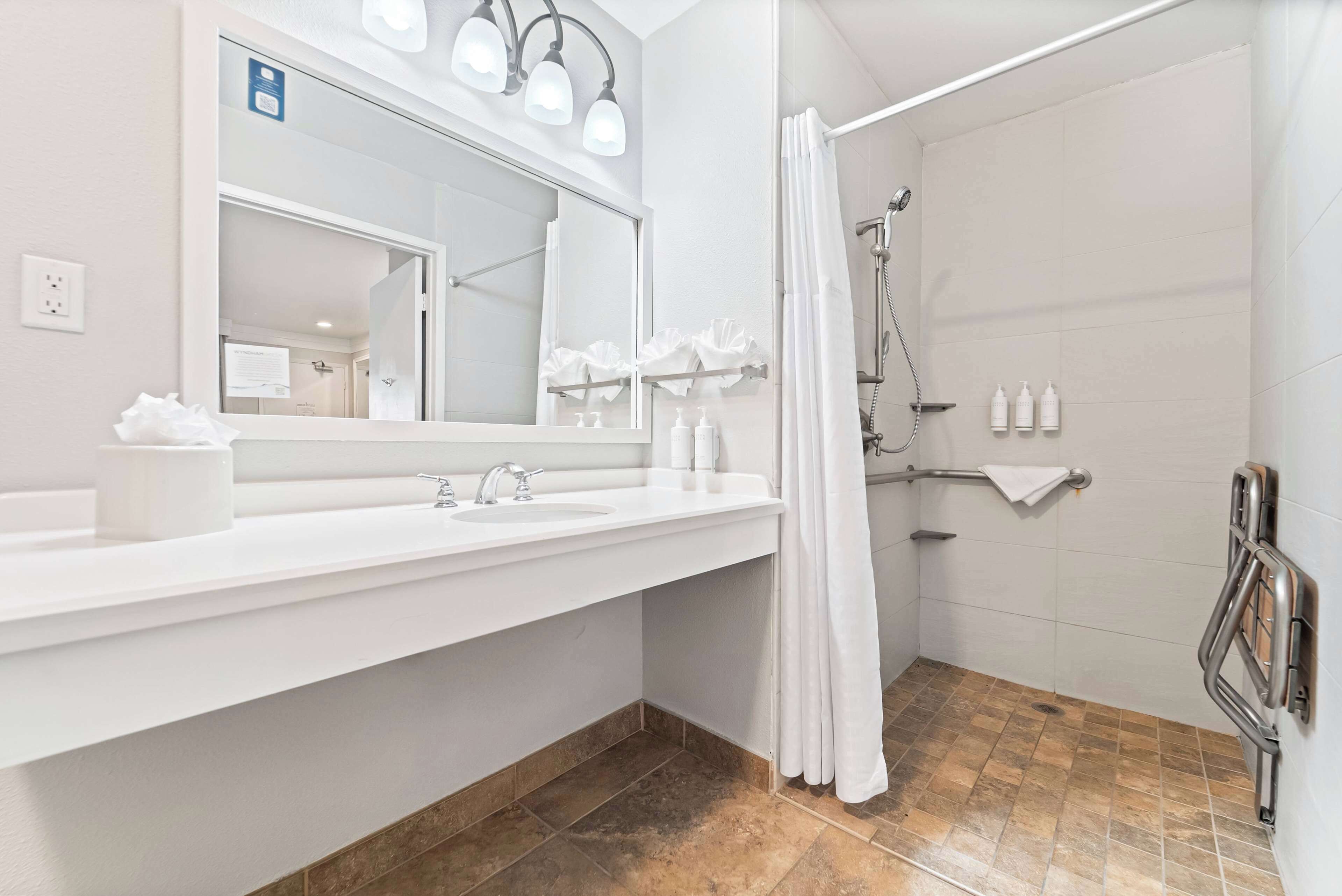 A modern bathroom with a large mirror, two sinks, a shower area, and a towel rack.