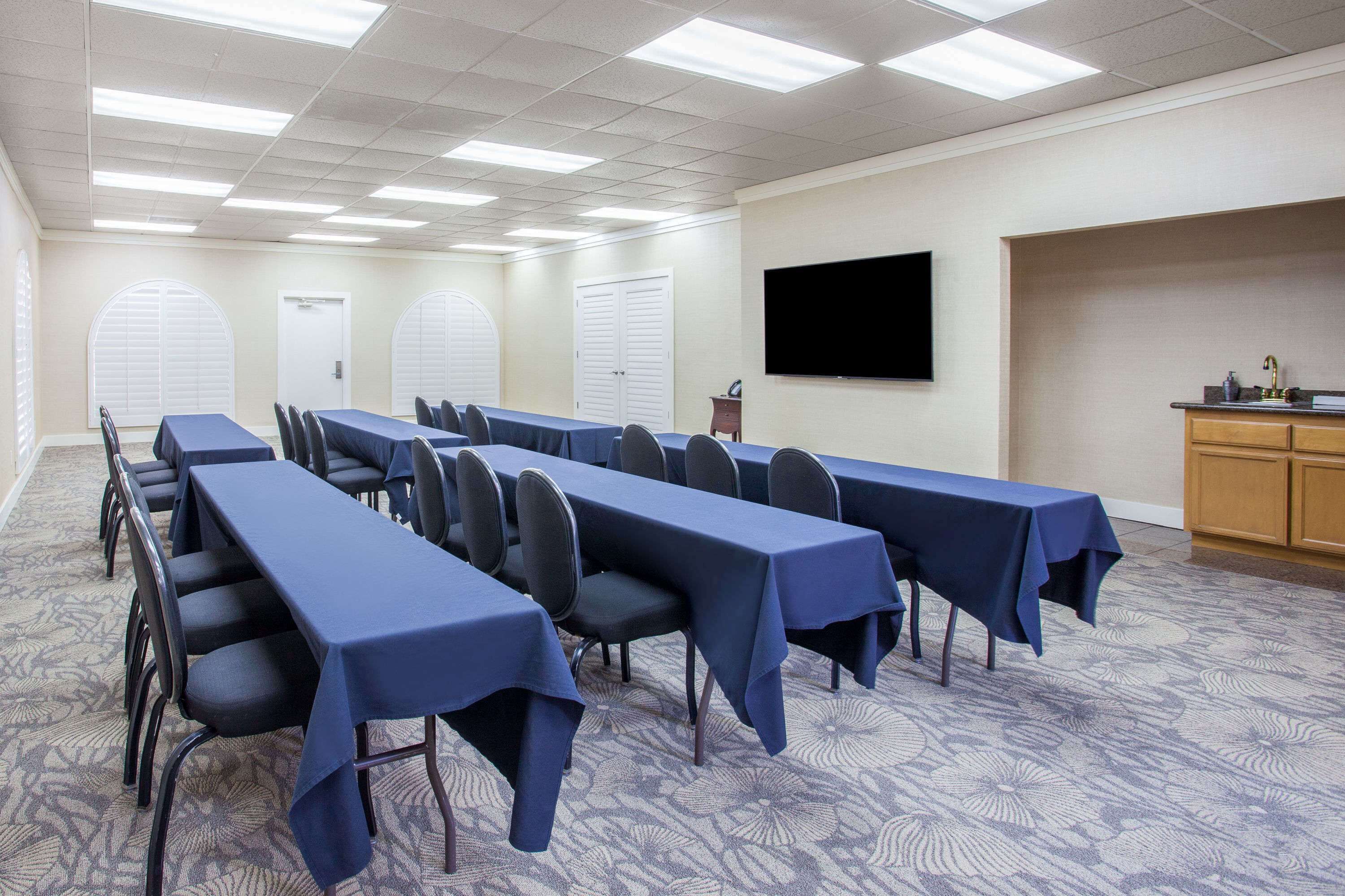 Un salón de conferencias con largas mesas, sillas, un televisor de pantalla plana y una kitchenette.