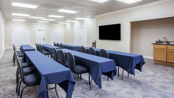 Un salón de conferencias con largas mesas, sillas, un televisor de pantalla plana y una kitchenette.