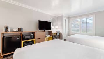 A hotel room with two beds, a television, a desk with a chair, a microwave, a refrigerator, and a window with blinds.