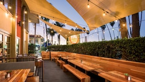 Un área de estar al aire libre con bancos y mesas de madera, un toldo sombreado y un letrero de restaurante.