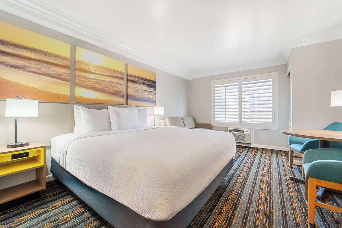 Ein Hotelzimmer mit einem großen Bett, einem Schreibtisch, einem Stuhl und einem Fenster mit Jalousien.