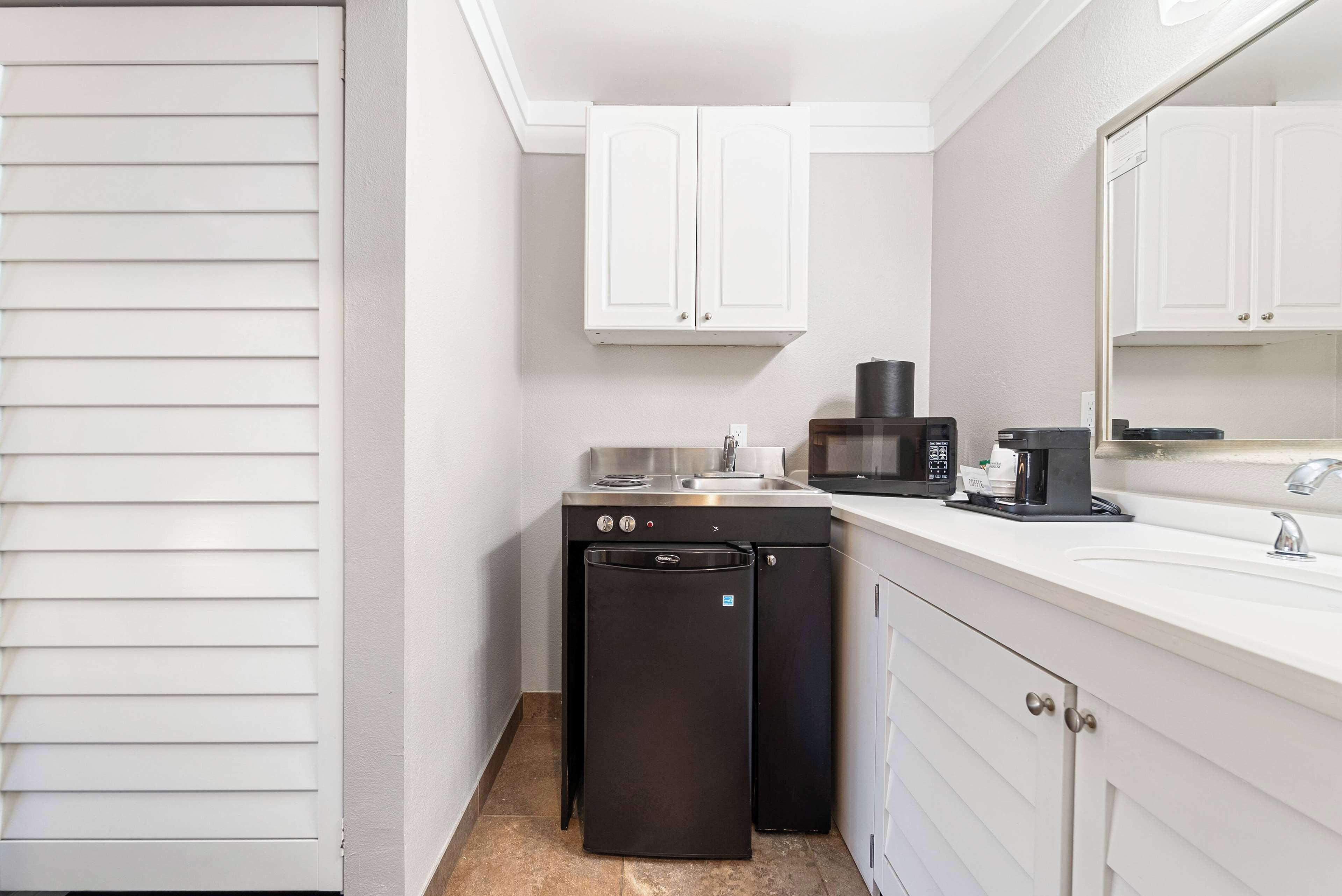 Una cocina compacta con armarios blancos, un refrigerador negro, un microondas y una cafetera.