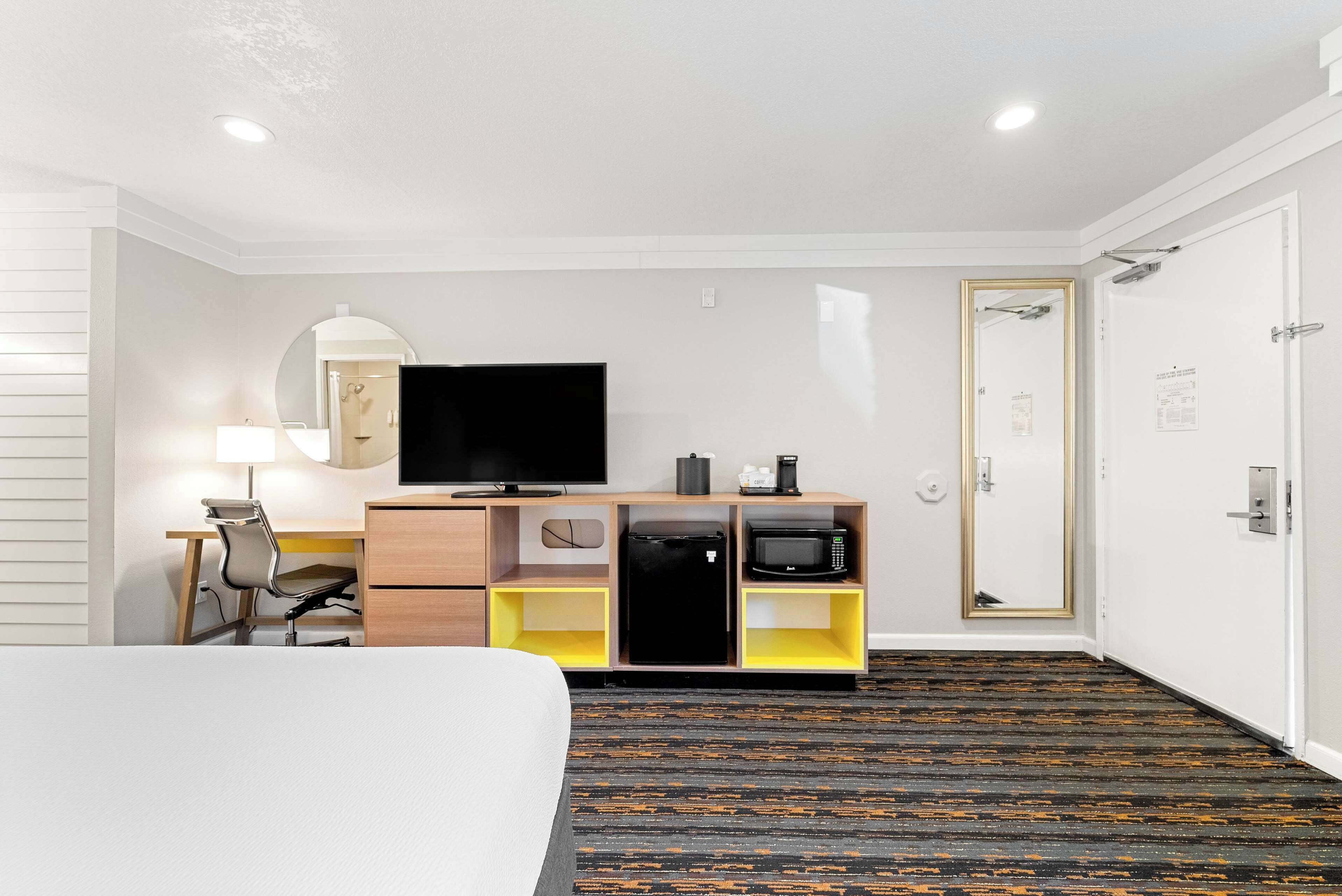 Habitación de hotel con cama, escritorio con silla, televisión, microondas y refrigerador pequeño.