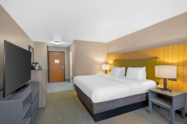 Una habitación de hotel con cama, mesitas de noche, televisor y puerta que da a un baño.