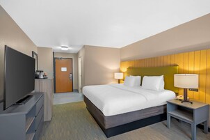 Una habitación de hotel con cama, mesitas de noche, televisor y puerta que da a un baño.