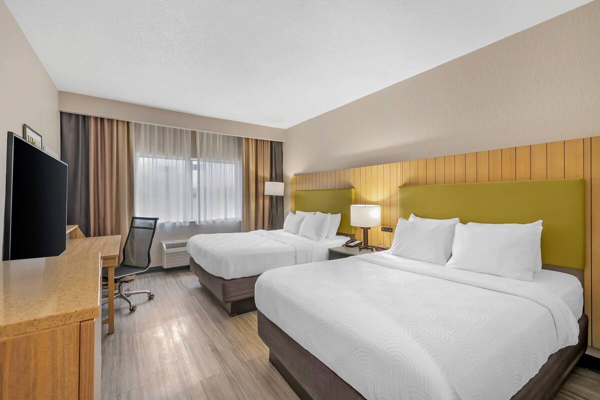 A hotel room with two beds, a desk, a TV, and a window with curtains.