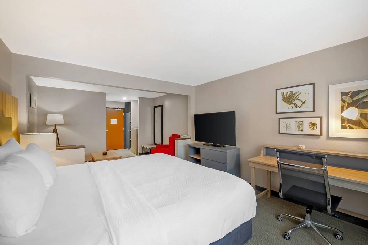 A hotel room with a large bed, a desk with a chair, a television, and artwork on the walls.