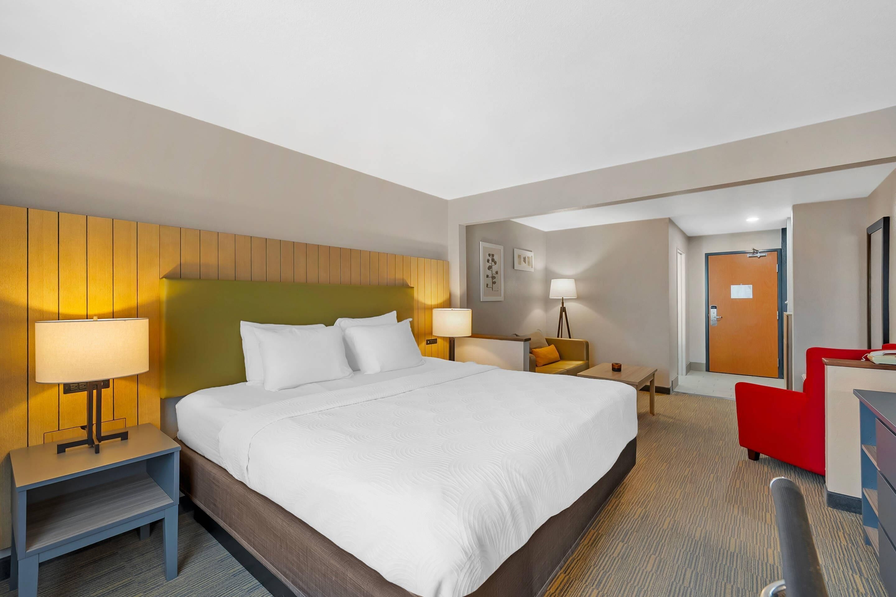 A hotel room with a large bed, bedside tables with lamps, a desk, a chair, and a door.