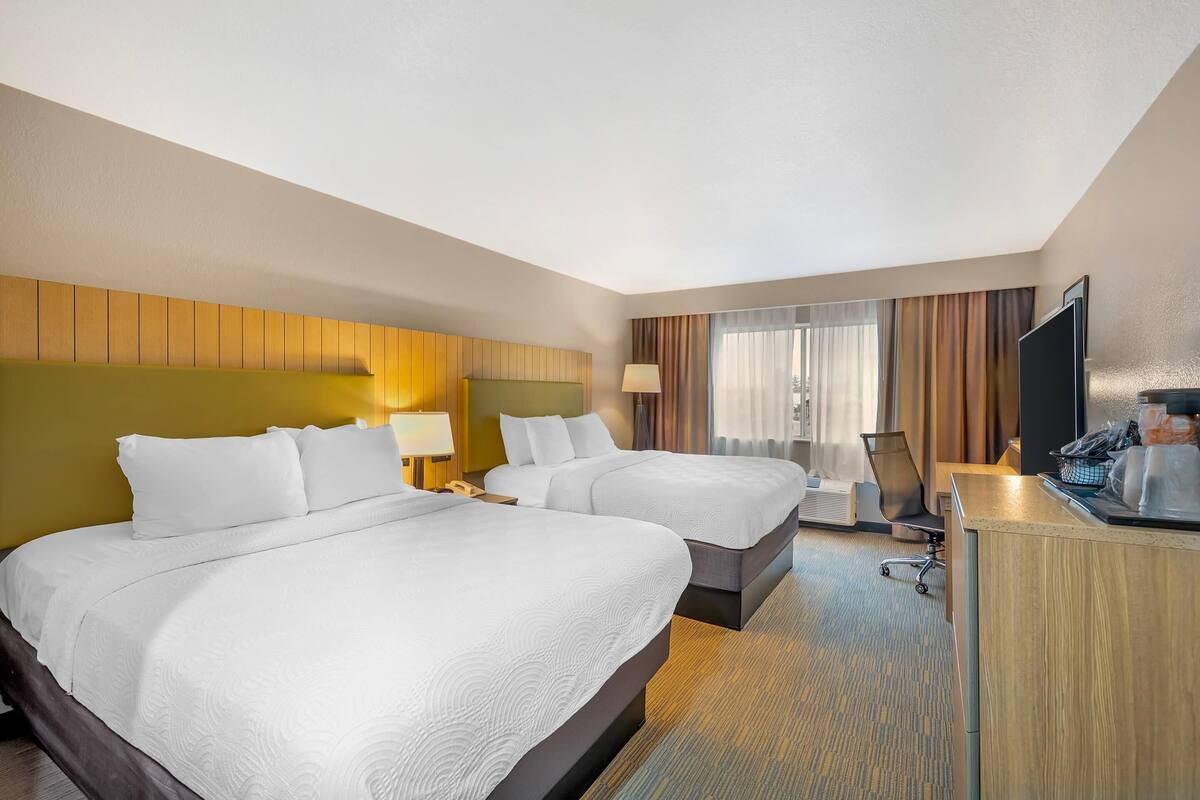 A hotel room with two beds, a desk, a chair, a TV, and a window with curtains.