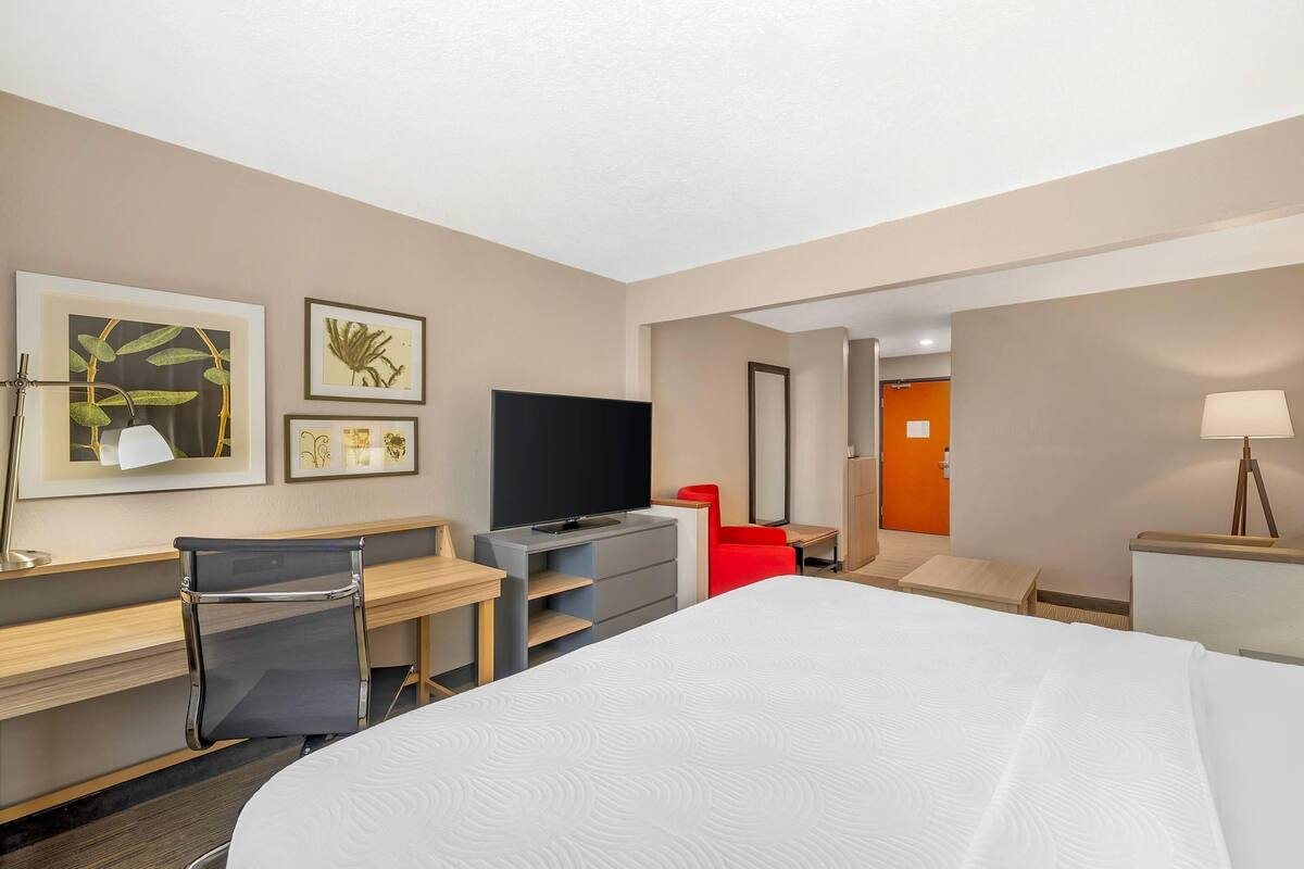A hotel room with a bed, desk, chair, television, and artwork on the walls.