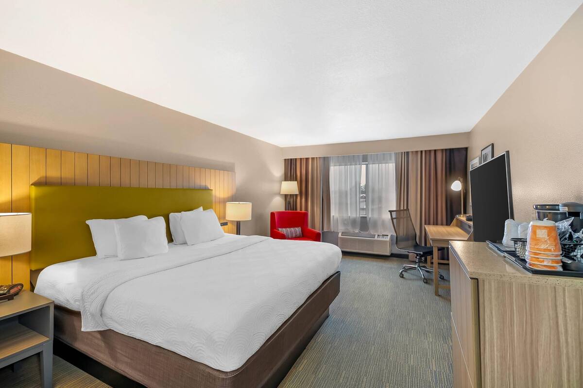 A hotel room with a large bed, a desk, a chair, a TV, and a window with curtains.