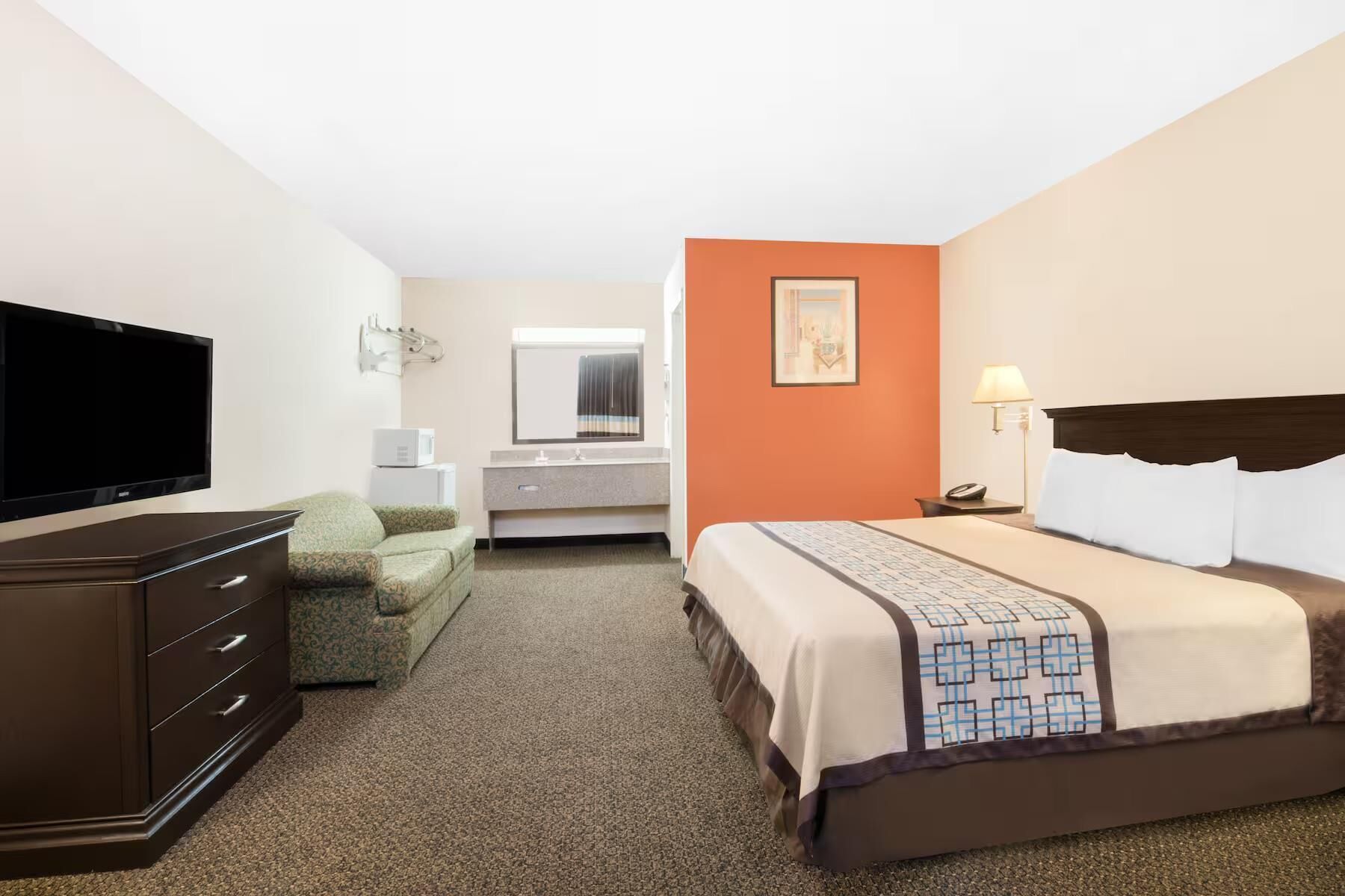 Habitación de hotel con cama, televisión, escritorio, silla y espejo de baño.