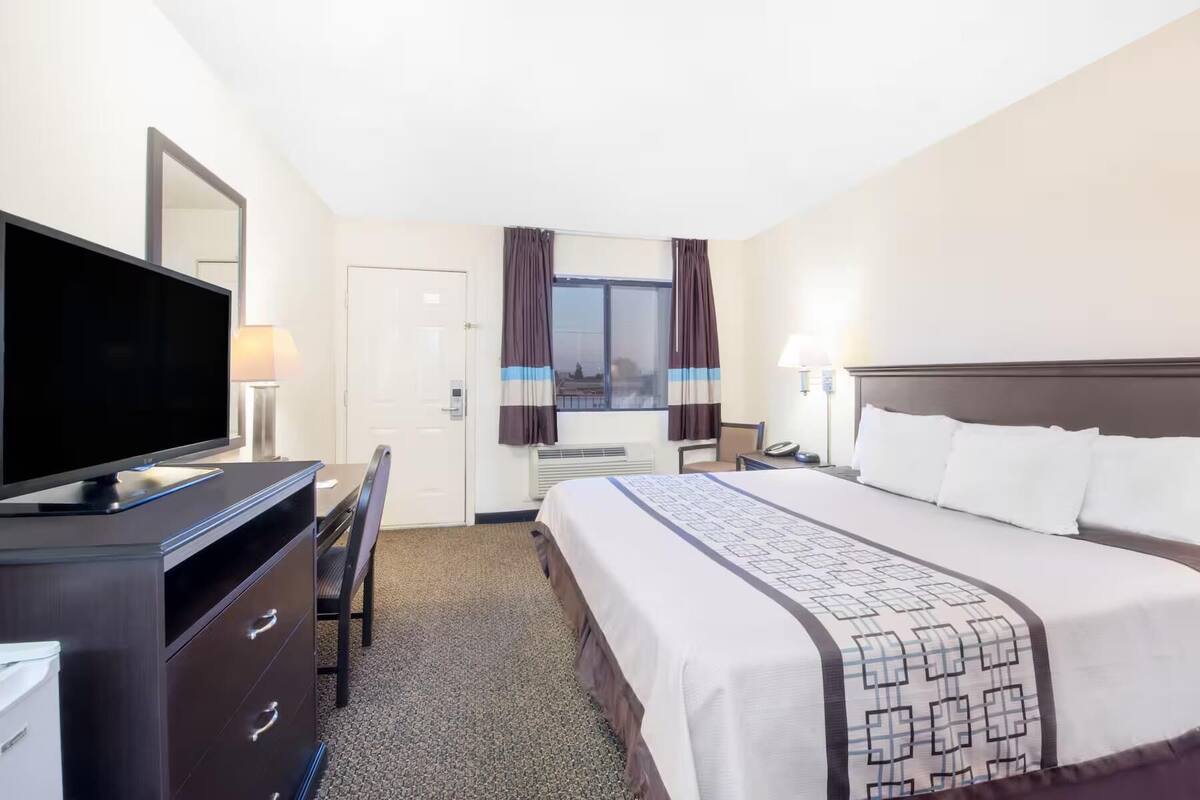 A hotel room with a bed, a desk with a computer, a TV, and a window with curtains.