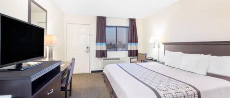 A hotel room with a bed, a desk with a computer, a TV, and a window with curtains.