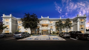 Un hotel gran de diverses plantes, amb una entrada imponent, múltiples places d'aparcament i un cel serè.