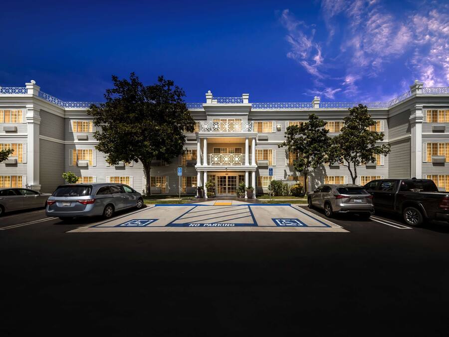 A large, multi-story hotel with a grand entrance, multiple parking spaces, and a clear sky.