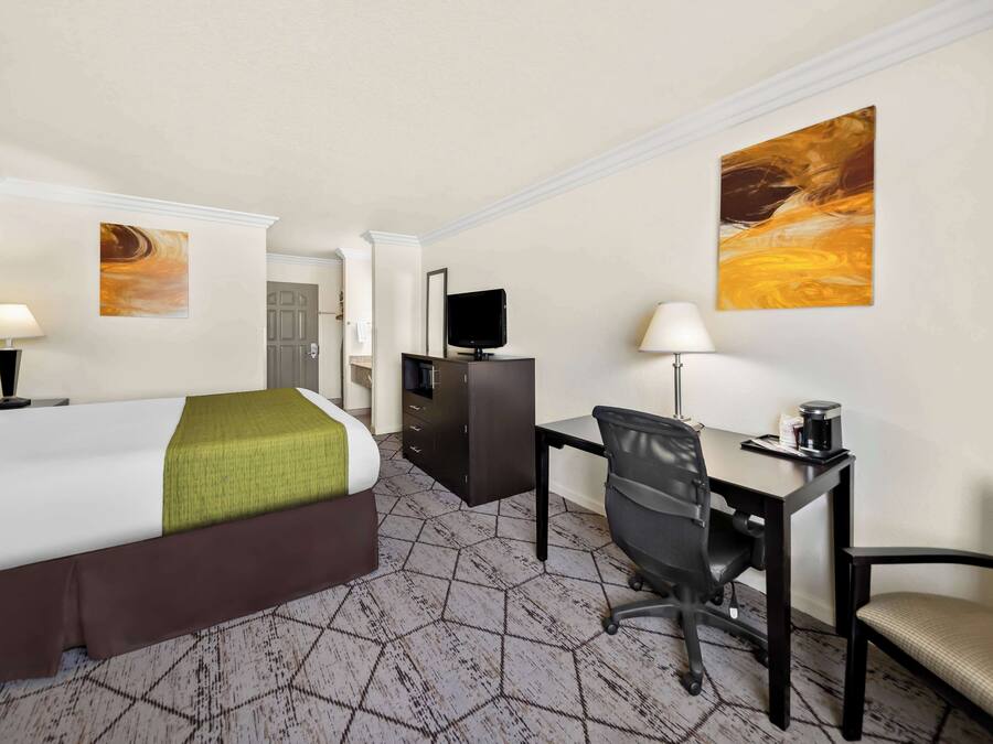 A hotel room with a bed, desk, chair, and a television.