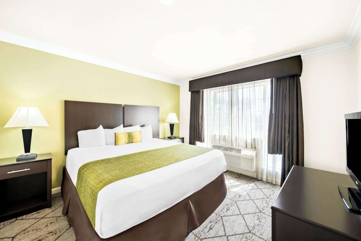A hotel room with a large bed, two bedside tables with lamps, a flat-screen TV, and a window with curtains.