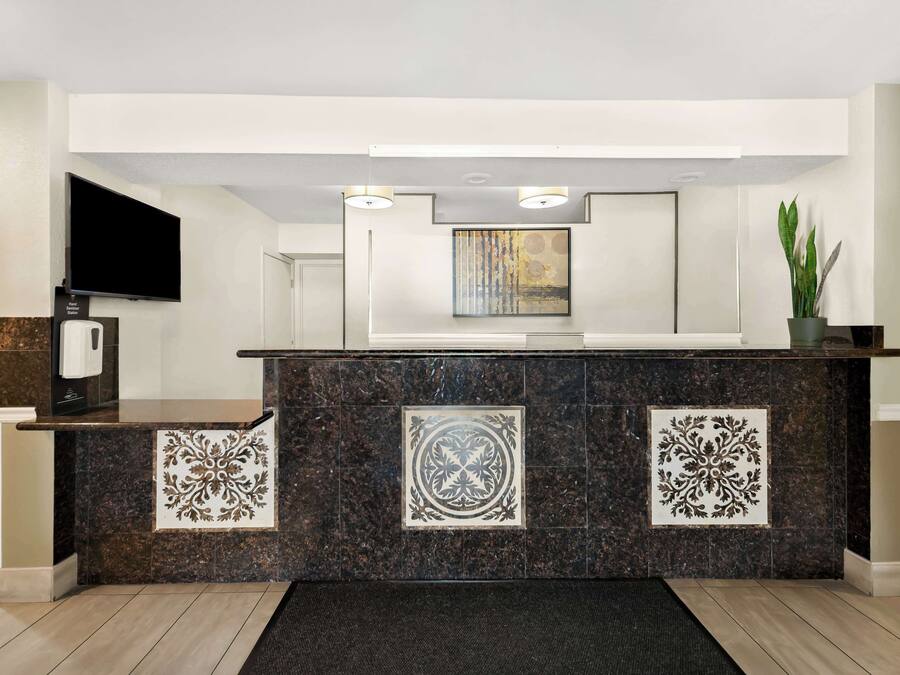 A reception area with a marble counter, a flat-screen TV, a coffee machine, and a potted plant.