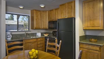 Une cuisine avec des meubles de rangement en bois, un réfrigérateur noir, un four à micro-ondes et une table à manger avec des chaises.