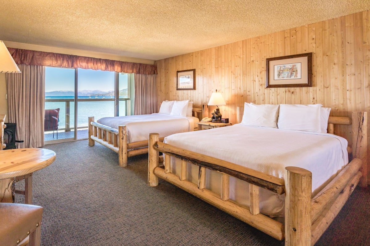A hotel room with two wooden beds, a small table, and a chair.