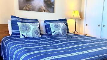 A hotel room with a large bed, two pillows, a nightstand with a lamp, and a painting on the wall.