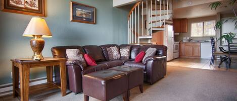 A living room with a brown leather sofa, a wooden side table with a lamp, and a framed picture on the wall.