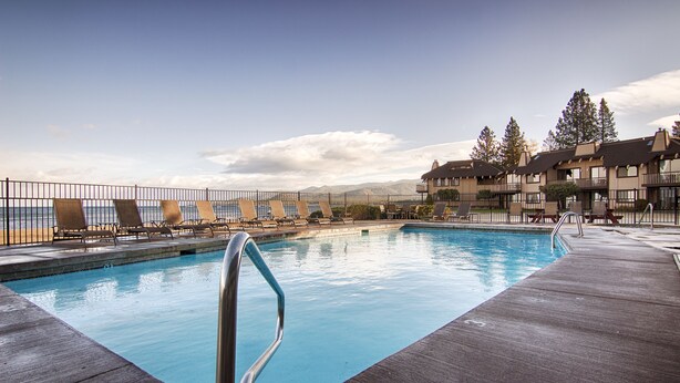 A swimming pool with a metal railing, lounge chairs, and a view of the ocean and mountains.