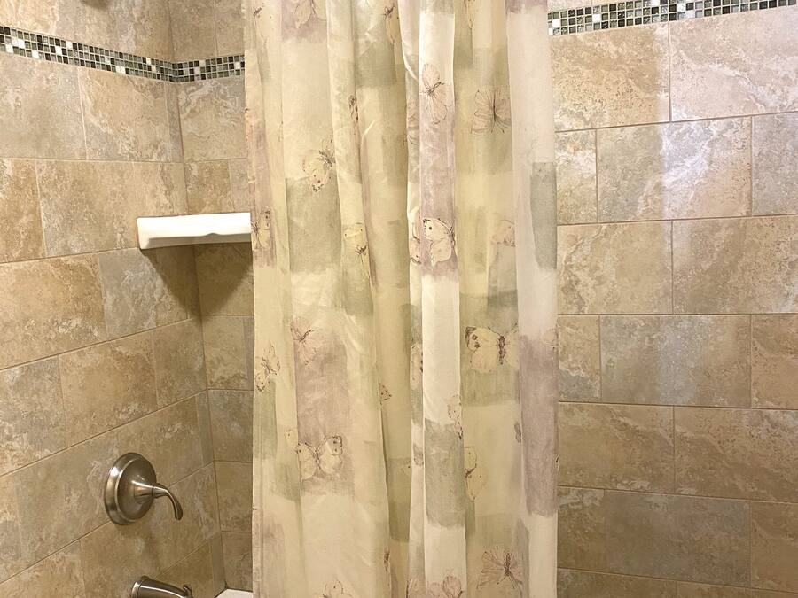 A bathroom with a bathtub, shower, and a curtain with a butterfly pattern.