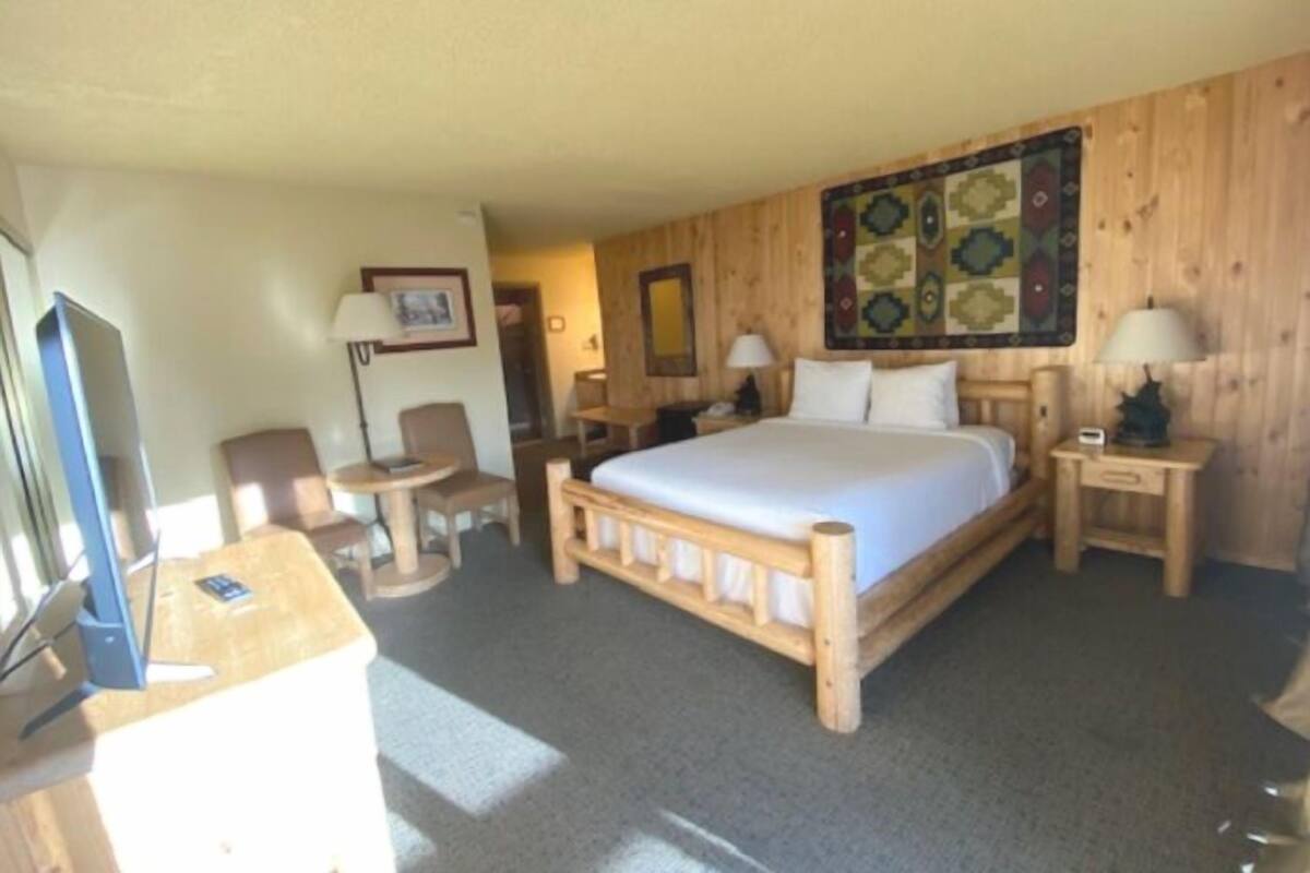 A room with a wooden bed, a desk with a computer, a chair, and a small table.