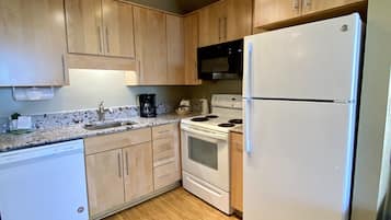 A compact kitchen with wooden cabinets, a white dishwasher, a stove, a microwave, and a refrigerator.