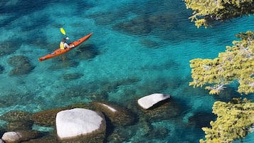 A kayaker in a clear blue sea with visible rocks and green vegetation.