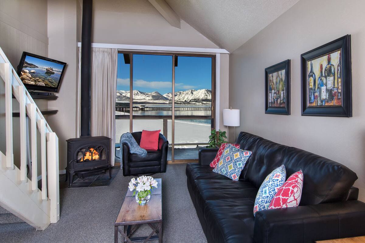 A living room with a fireplace, a sofa, a chair, a table with flowers, and a TV on the wall.