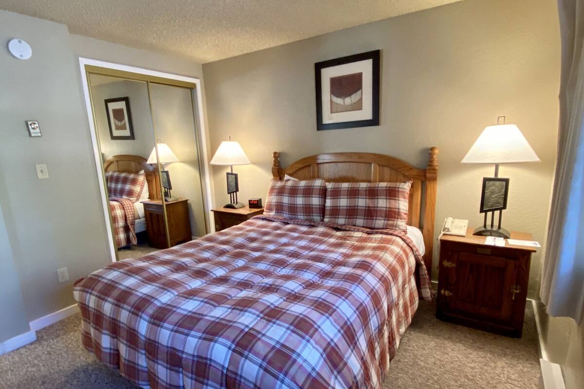 A bedroom with a bed, two bedside tables, a mirror, and a wall-mounted picture.
