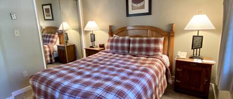 A bedroom with a bed, two bedside tables, a nightstand, a mirror, and a framed picture on the wall.