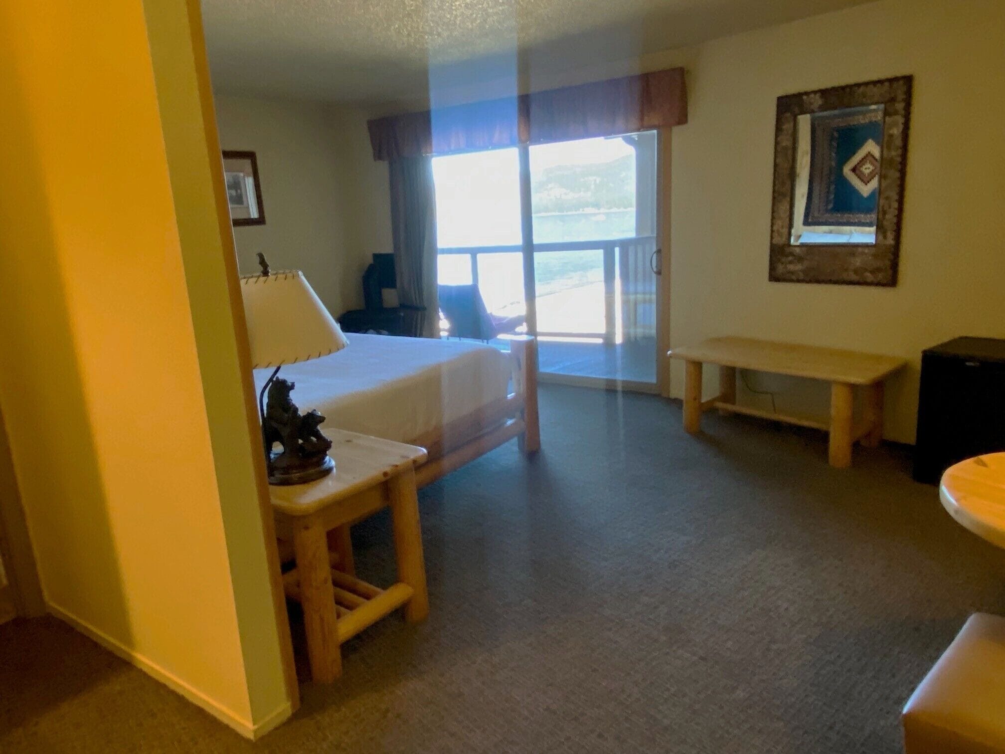 Habitación de hotel con cama, escritorio, banco y vistas al exterior a través de un gran ventanal.