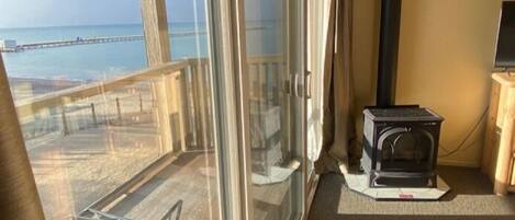 Un balcón con puerta de vidrio, un pequeño calentador y vista a la playa.