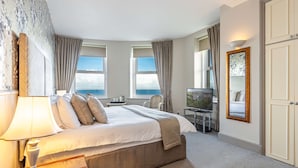 Une chambre d’hôtel avec un grand lit, un bureau avec une chaise, une télévision et une vue sur la mer.