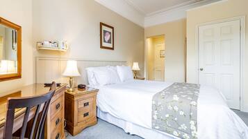 Een hotelkamer met een bed, een bureau, een stoel, een nachtkastje met lampen, een wandplank met toiletartikelen en een deur.