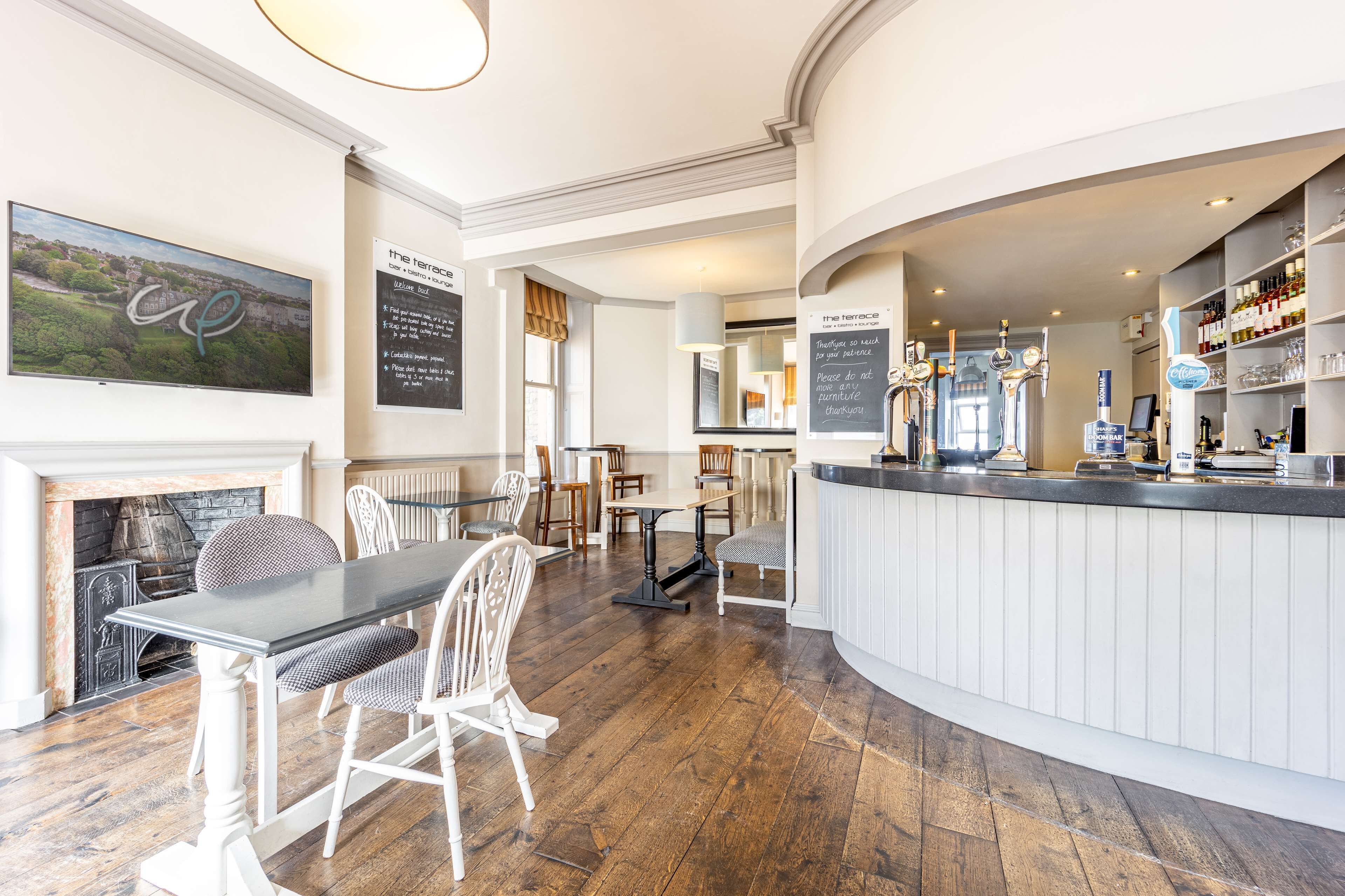 A restaurant with a bar area, wooden flooring, white furniture, and a fireplace.
