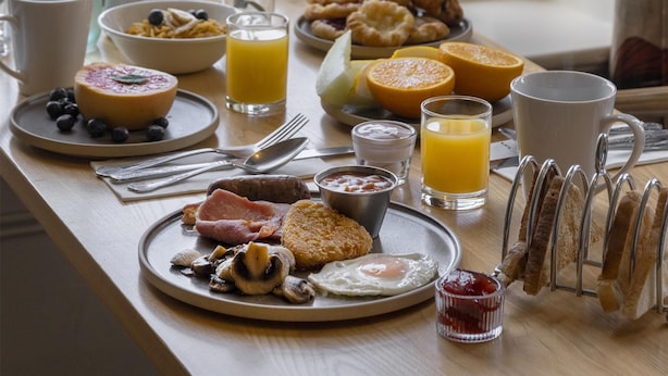 Une table de petit-déjeuner avec divers aliments et boissons, une bouteille, et une vue sur la mer.
