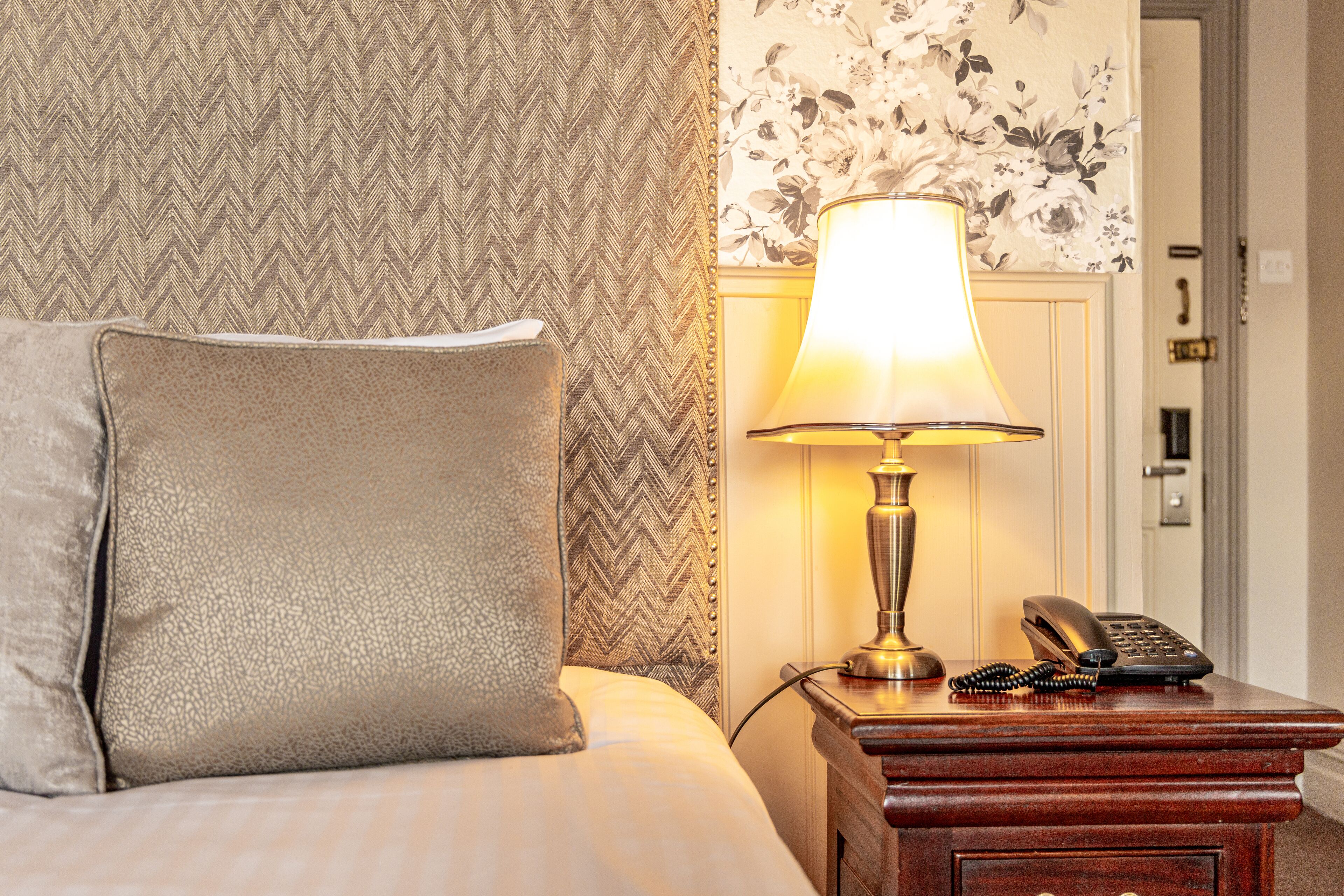 A neatly made bed with a pillow, a bedside lamp, and a telephone on a wooden nightstand.
