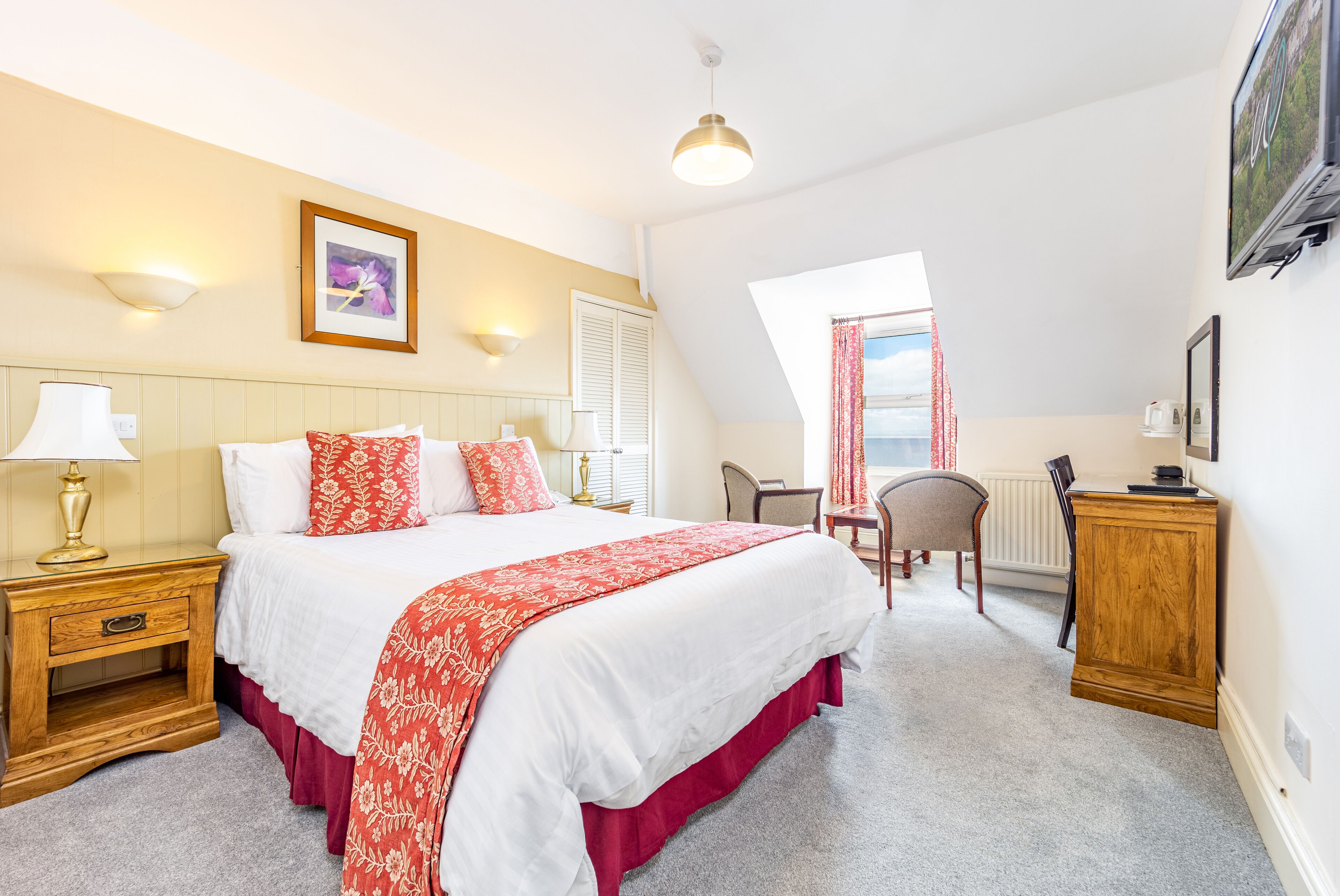 A bedroom with a large bed, a nightstand, a chair, a desk, and a window with curtains.