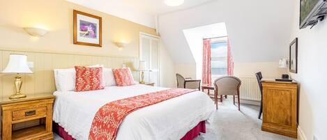 A bedroom with a large bed, a nightstand, a chair, a desk, and a window with curtains.