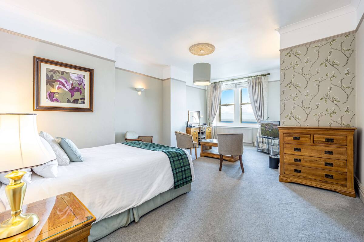 A hotel room with a bed, desk, chair, dresser, and a framed picture on the wall.