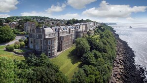 Un grand bâtiment historique à étages, situé sur une colline surplombant une côte rocheuse.